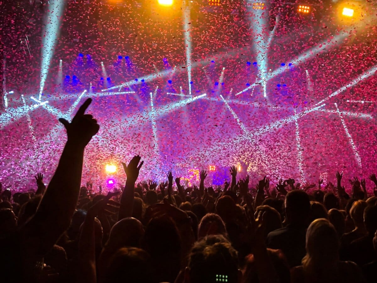 A concert crowd with hands raised under bright stage lights