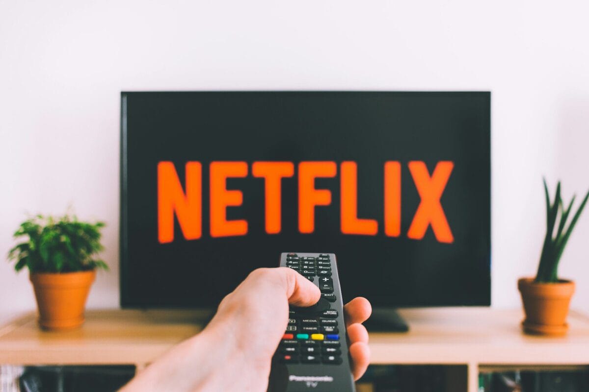 A hand holding a TV remote control in a dark living room